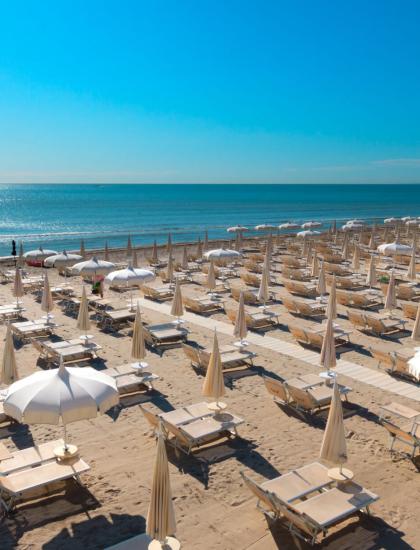Strand mit Liegen und Sonnenschirmen, ruhiges Meer und klarer Himmel.